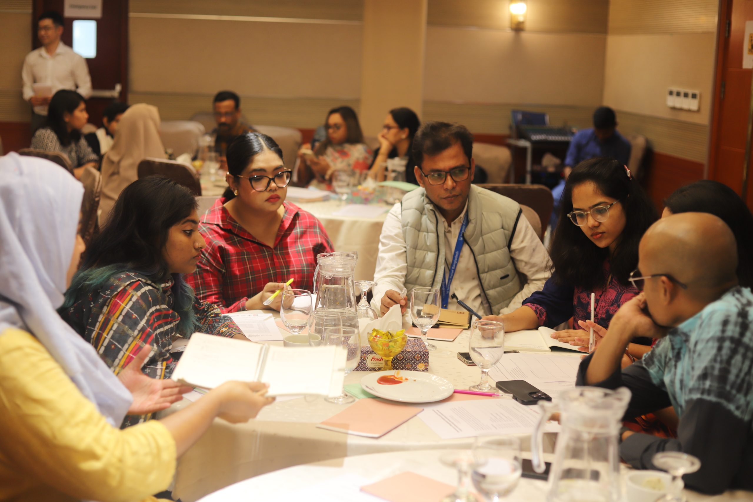 Groups of people in discussion are seated at round tables