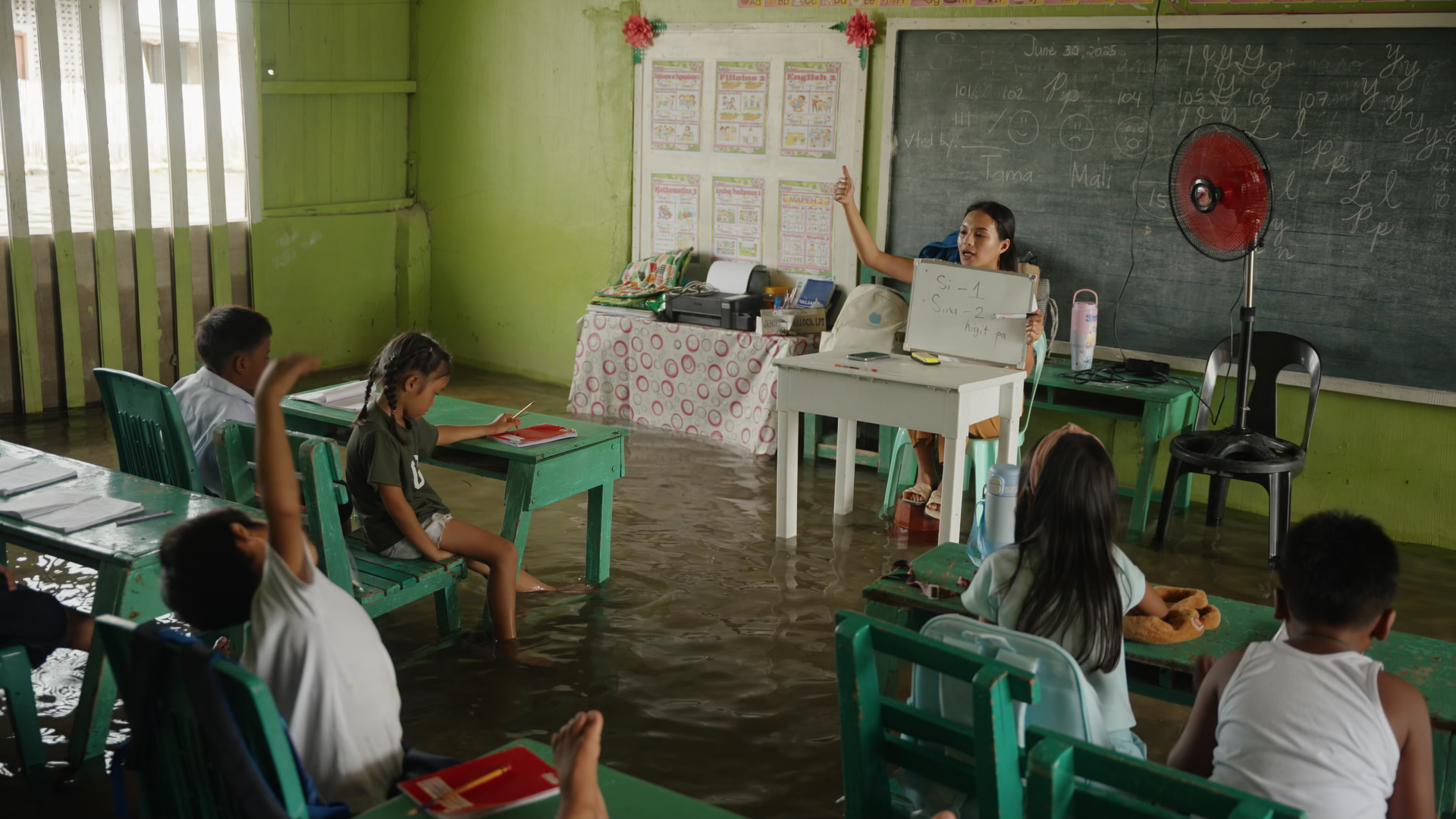 Children and a teacher in a classroom with water covering the floor.